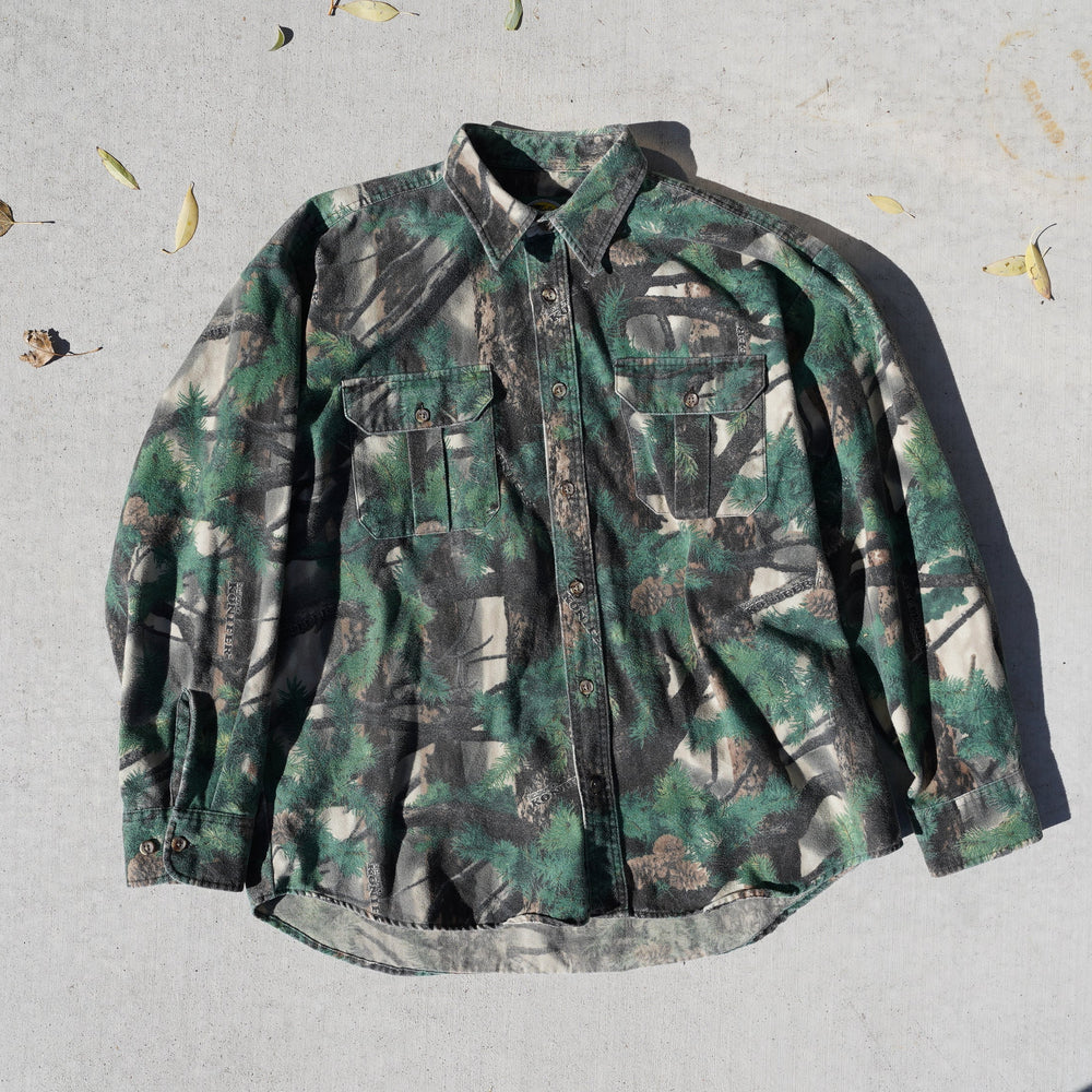 Camouflage jacket on a light gray surface with scattered leaves.