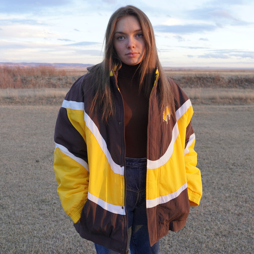 90s Wyoming Cowboys Apex One Wave jacket in brown, gold, and white color blocking, size L–XL, modeled outdoors. Vintage sourced, cleaned, and restored in Wyoming. West Block Vintage.