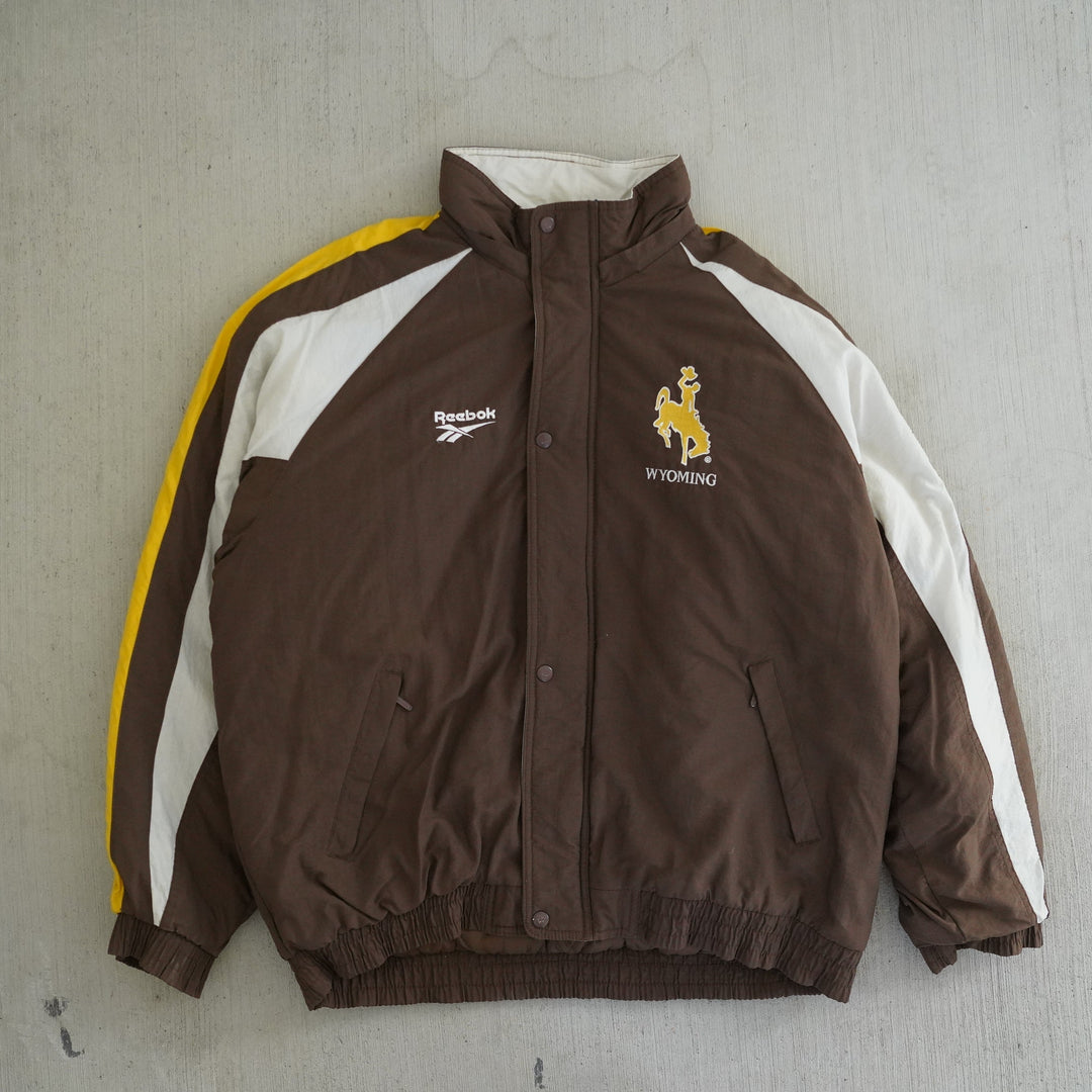 Vintage 1990s Reebok Pro Line Wyoming Cowboys jacket in brown, gold, and white with embroidered logos and large back graphic — Vintage Wyoming Gear Collection, West Block Vintage.