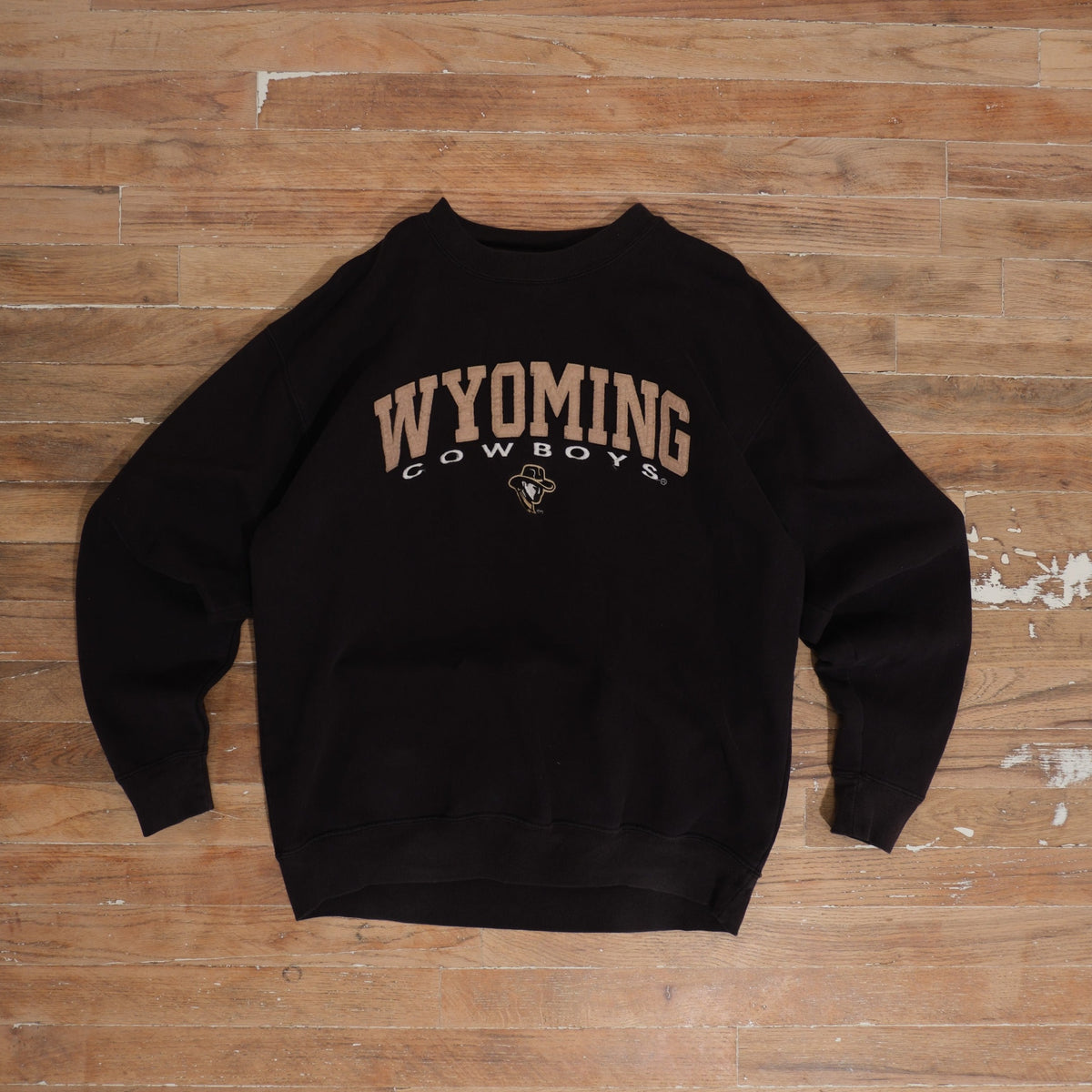 Y2K faded black Wyoming Cowboys Black Arched Logo Crewneck photographed flat on wood floor