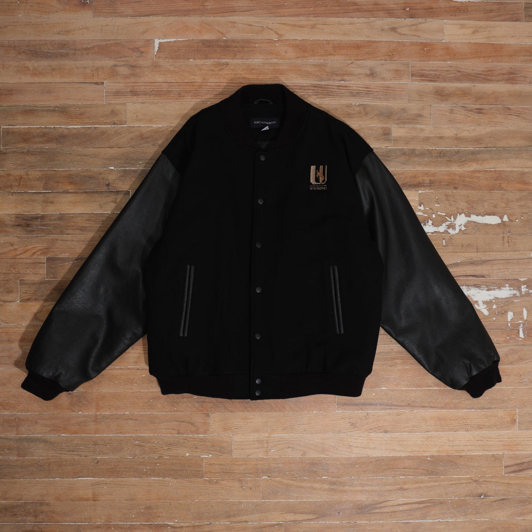 Y2K black / brown / cream Wyoming Cowboys Black Leather Sleeve Varsity Jacket photographed flat on wood floor