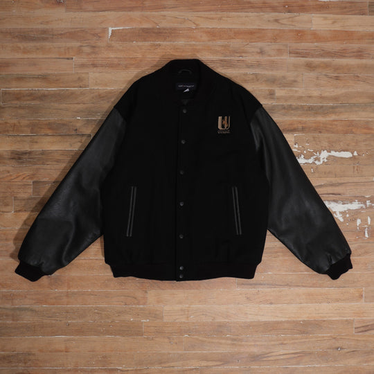 Y2K black / brown / cream Wyoming Cowboys Black Leather Sleeve Varsity Jacket photographed flat on wood floor