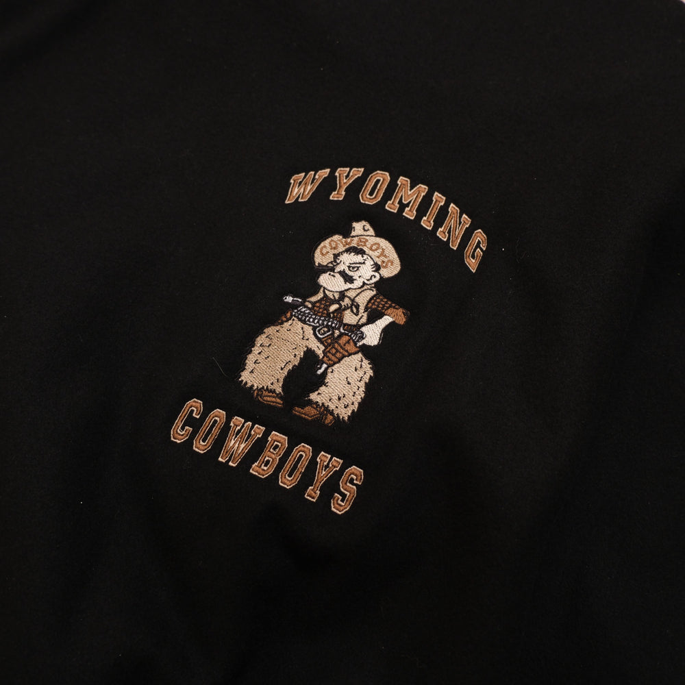 Y2K black / brown / cream Wyoming Cowboys Black Leather Sleeve Varsity Jacket photographed flat on wood floor front detail