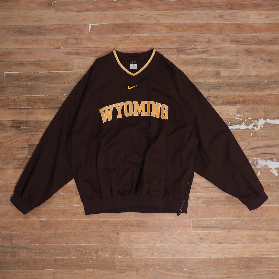 Mid-2000s Nike Wyoming Cowboys brown V-neck windbreaker with gold center Swoosh, arched Wyoming lettering, white and gold collar trim, and front pockets.