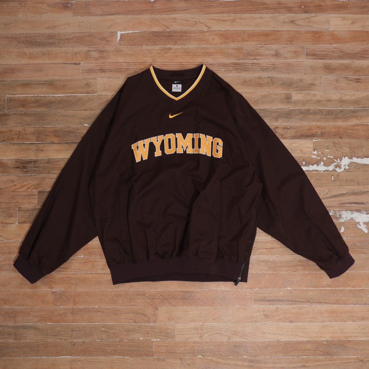 Mid-2000s Nike Wyoming Cowboys brown V-neck windbreaker with gold center Swoosh, arched Wyoming lettering, white and gold collar trim, and front pockets.