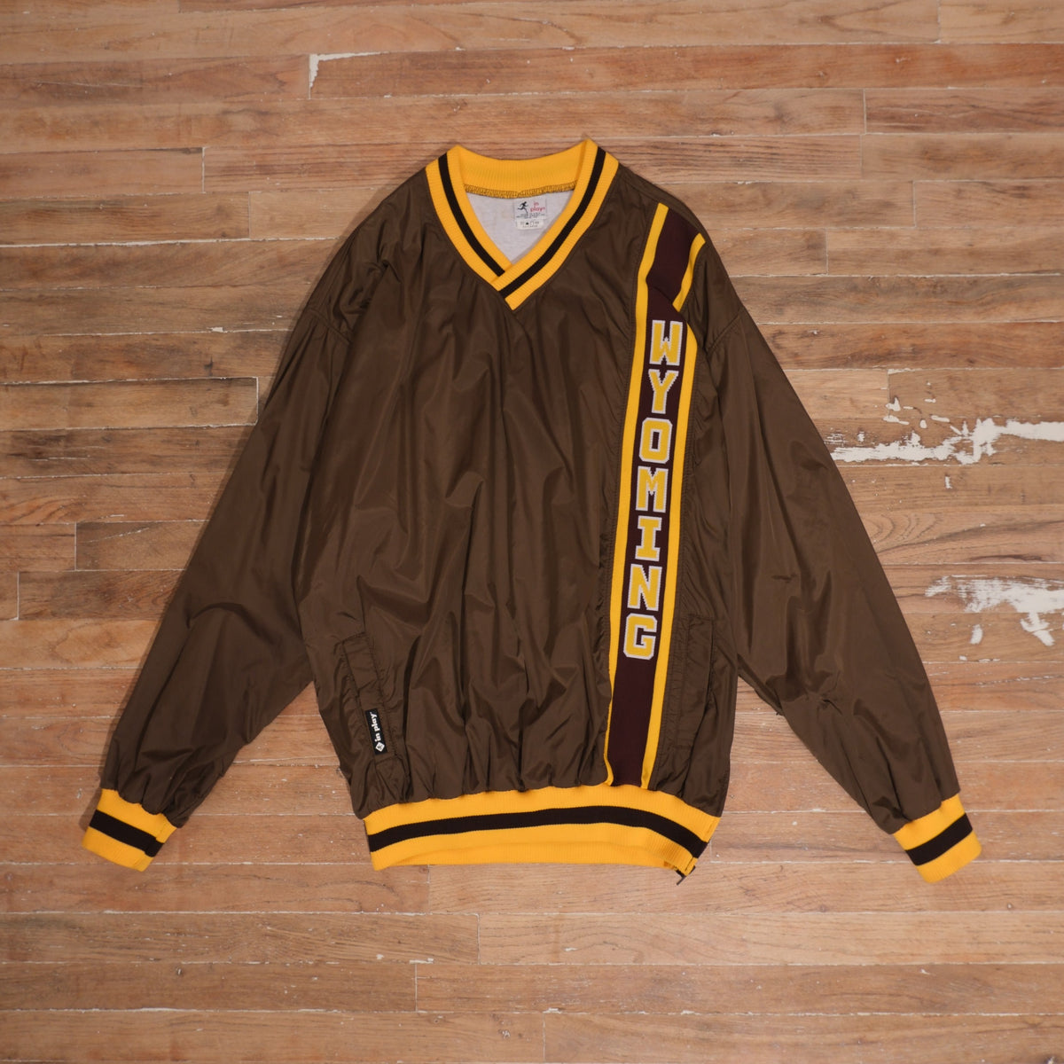 Vintage 1980s Wyoming Cowboys brown V-neck tracksuit windbreaker with vertical gold Wyoming lettering, striped ribbed collar, cuffs, and waistband.